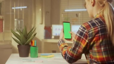 Genç bir kadının arka görüntüsü yeşil ekran cep telefonuna dokunuyor. Renkli kareli gömlekli bir kadın yönetici, tasarımcı ya da programcı. Metnin veya resmin için şablon yeri, promosyon