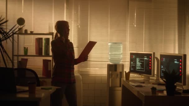 一个女人的轮廓是在手机上说话 并在平板文件夹中查看信息 经理晚上工作在一间黑暗的办公室里 靠近一个有背光的大窗户 办公室 — 图库视频影像