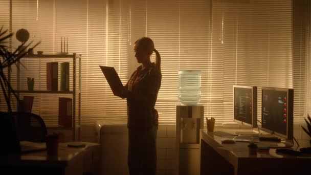 一个女人的轮廓是通过平板文件夹中的信息 并用钢笔做笔记 经理晚上工作在一间黑暗的办公室里 靠近一个有背光的大窗户 办公室 — 图库视频影像