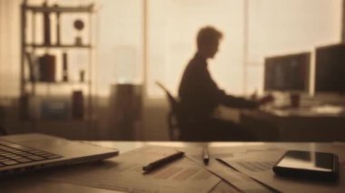Genç bir adamın bilgisayar klavyesine yazı yazarken ve akşamları karanlık bir ofiste kahve içerken bulanık bir silueti. Yönetici arka lambalı bir pencerenin yanındaki masada oturuyor. Ofis işi