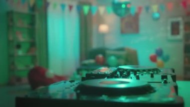 Ev partisi ya da doğum günü için dekore edilmiş bir odanın içi. Erkek eller kulaklıkları alır ve DJ konsolunda müziği karıştırır. Oda balonlarla, aynalı disko topu ve bayraklarla süslenmiş. Konsept