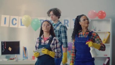 Mavi tulumlu çok uluslu bir temizlikçi grubu bir odayı teftiş ediyor ve dijital tablet kullanarak partiden sonra ofis temizliği yapmayı planlıyor. Temizlik hizmeti konsepti. Bir sürü çöp var.