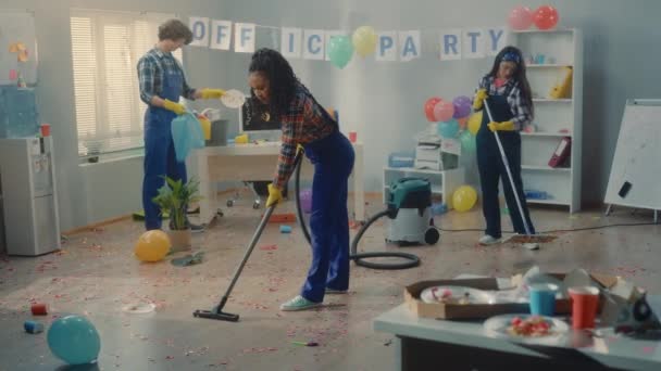 企業パーティーの後にオフィスを清掃する多国籍グループ アフリカ系アメリカ人の女性アジア系の女性とヨーロッパ系の男性がゴミ袋に入れて床を掃き掃除しゴミを収集します — ストック動画