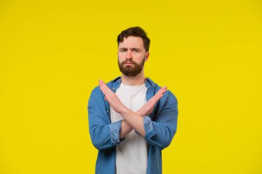 İzole edilmiş stüdyo sarı arka planda x çapraz el hareketi yaparak anlaşmazlık gösteren genç yakışıklı adamın portresi