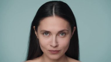 Genç, beyaz bir kadın iki elini de gözünün altında gezdiriyor. Mavi arka planda bir kadının yüzünü kapat. Yüz masajı, cerrahi yenilenme, kırışıklık önleyici, yaşlanma önleyici konsept