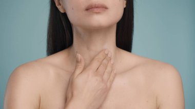Bir kadın boynuna krem sürüyor. Yavaş masaj hareketleriyle, bir kadın kremi cildine sürterek mavi bir arka plan oluşturur. Cilt ve vücut bakımı kavramı. Doğal güzellik.