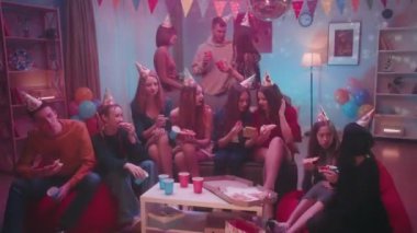 Bir evde kutlama şapkası takan gençler pizza yer, kağıt bardaklardan içer, iletişim kurarlar. Kız, telefon videosundaki arkadaşlarını gösteriyor. Odanın içi diskosu olan bir parti için dekore edilmiş.