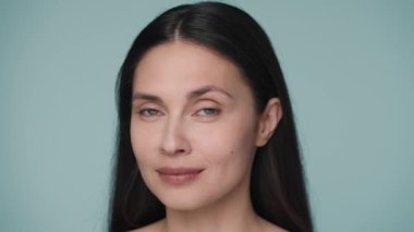 Temiz, sağlıklı cilde sahip genç bir kadın kameraya bakar ve öpücük yollar. Mavi arka planda güzel bir kadının portresi. Doğal güzellik, yüz bakımı, kozmetoloji. Yavaş çekim