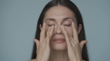 Genç bir kadın yüzüne nazik hareketlerle masaj yapar. Mükemmel pürüzsüz bir teni olan genç ve güzel bir kadının yüzü. Mavi arka planda soyutlanmış. Doğal güzellik, estetik ameliyat.