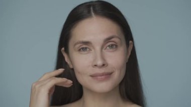 Genç bir kadın manikürlü elleriyle çenesini kapatıyor ve yüzünü sağa sola çeviriyor. Kadın doğru yüz hatlarını yakından gösteriyor. Doğal güzellik, yüz bakımı, kozmetoloji, plastik