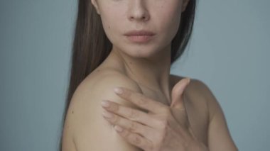 Yavaş masaj hareketleriyle, kadın kremi omzuna sürüyor. Bir seminer kadını mavi arka planda cildine dikkat eder. Cilt ve vücut bakımı kavramı. Doğal güzellik. HDR