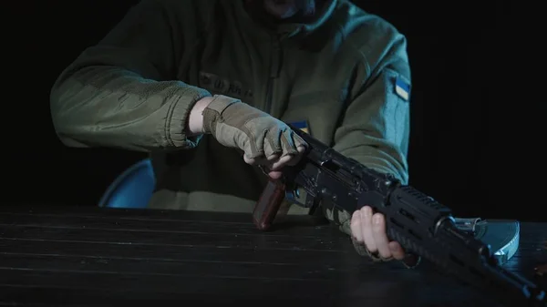 乌克兰武装部队的一名士兵手里拿着一支卡拉什尼科夫冲锋枪坐在一张桌子旁 士兵的手紧紧抓住来福枪的安全 — 图库照片