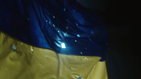 スポットライトに照らされた黒い背景にウクライナの発展途上の青い黄色の旗 弾丸の穴で覆われたウクライナの旗を閉じる ウクライナと — ストック写真