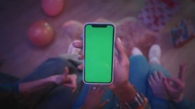 Kucağında yeşil ekran telefon tutan Afrikalı Amerikalı kadınların elleri. Bir kız bir şey gösterir, arkadaşlarına telefon eder, kızlar işaret parmaklarıyla işaret eder, baş parmağını kaldırır.