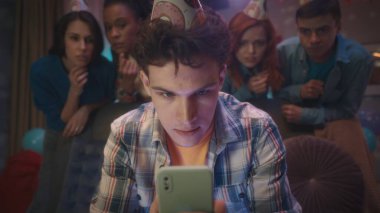 Adamın biri telefonuyla oyun oynuyor. Arkadaşları da onu gergin bir şekilde arkasında izliyor. Oyunlar, ev partilerindeki eğlence / Kapat