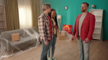 Bir emlakçı bir daireyi birkaç kişiye gösterip, yararları hakkında konuşur. Erkekler el sıkışır, bir anlaşmayı kutlar, profesyonel hizmet için teşekkür ederler. Bir erkeğin tokalaşmasına yakın.