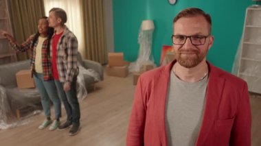 Emlakçı dairenin anahtarını gösteriyor ve onayını veriyor. Oturma odasında bir adamın portresi mutlu bir çiftin arka planına karşı. Dairenin satışı ya da kiralanması