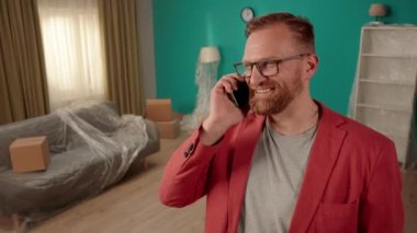Kendine güvenen bir emlakçı, yeni bir dairede duruyor ve potansiyel müşterilerle telefonda konuşuyor. Kulağının yanında telefonu olan bir emlakçı. Modern elektronik aletler ve iş. Yavaş çekim
