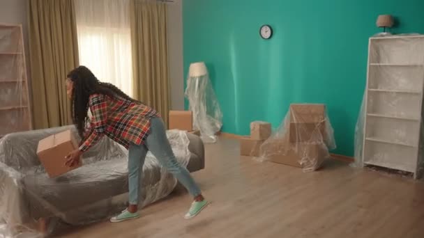 一个非裔美国女孩提着一个纸板箱走进客厅 年轻的心满意足的女孩在检查新公寓 购买财产 — 图库视频影像
