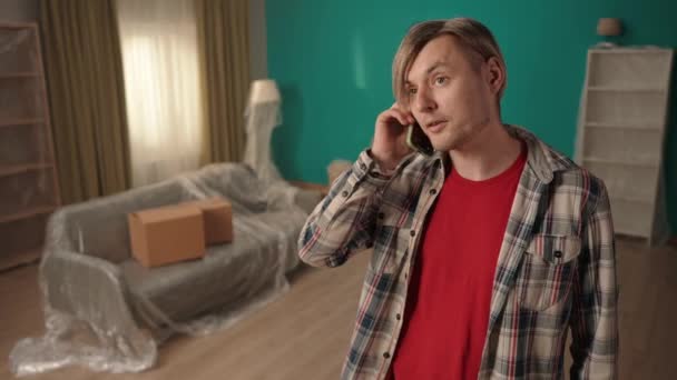 站在客厅里的那个人在电话上骂人 一个金发碧眼的男人在电话中感情用事的形象 令一个年轻人不满的是这一收购 一个有缺陷的公寓 — 图库视频影像