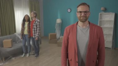 Bir emlakçı dairenin anahtarını gösteriyor ve onaylıyor. Arka planda evli ve mutlu bir çiftle oturma odasında duran kırmızı ceketli bir adamın portresi. Satış ya da kiralama