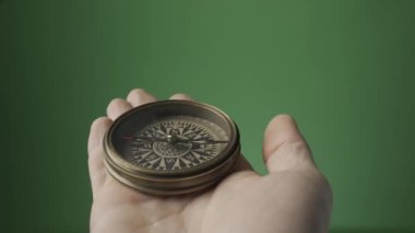Yeşil ekranda bir adamın elinde dönen bir ok olan klasik bir pusula. Pusula iğnesi kuzeyi gösteriyor. Turistler için ekipman. Seyahat ve Eğlence Endüstrisi. HDR BT2020 HLG Malzemesi