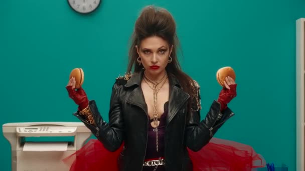 彼女の腕の中にハンバーガーを保持オフィスに立つフリーク女性 女は両方のハンバーガーから噛み合わせ 彼女の口をいっぱいに詰め込んで貪欲になります 食事の拒否 不健康な食品 — ストック動画