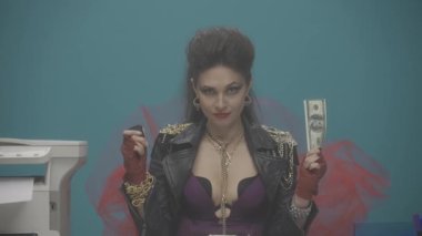 Ofisteki bir masada elinde para olan bir kadın oturuyor. Kız bir dolarlık banknota benzin çakmağı getirip yakıyor. Para değerinin düşmesi. Lanet olsun. İtiraz ediyorum. Feminizm. Reklamcılık