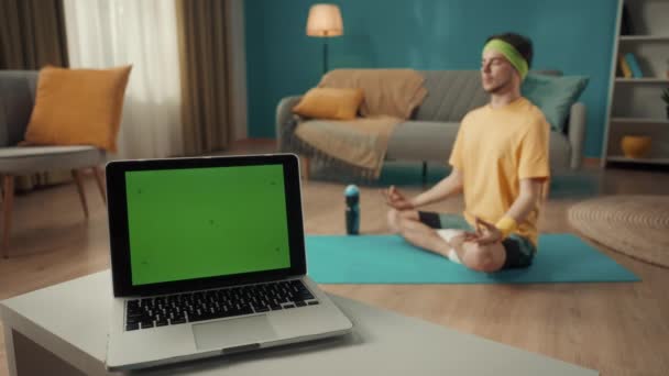 客厅的桌上放着有绿色屏风的笔记本电脑 在后面 一个男人坐在一个荷花的位置上 体育概念 瑜伽课 您的文字 促销内容的模板位置 — 图库视频影像