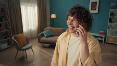 Genç bir adam akıllı telefondan konuşuyor. Müdahaleciye evinden bahsediyor. İşaret parmağıyla mobilyaları işaret ediyor. Oturma odasında kulağına telefon dayanmış kıvırcık saçlı bir adamın portresi.