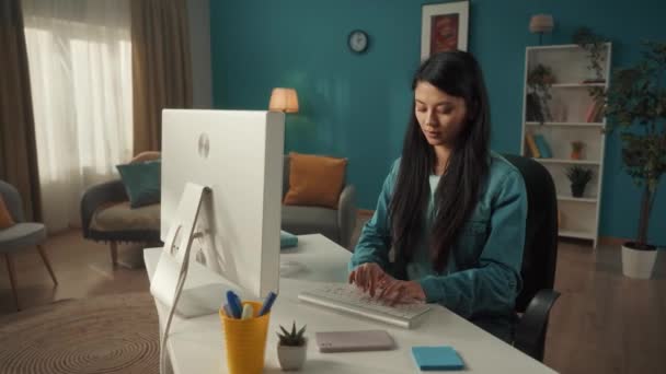 若いアジアの女性がコンピュータに座っている間にスマートフォンで話しています 女性は会話を終了し キーボードを入力し メッセージを書き チャットし フリーランスになる — ストック動画