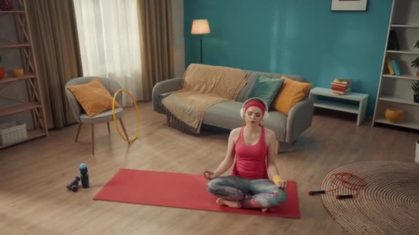 Рыжая Молодая Женщина Наушниках Сидит Позе Лотоса Медитирует Практикует Йогу — стоковое видео
