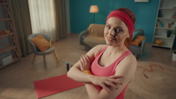 一个红头发女人的画像 她交叉着胳膊 看着相机笑了 一个穿着运动服的女人 靠着客厅的后面 有训练的特征 — 图库视频影像