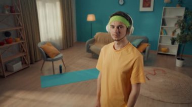 Ev çalışmasından sonra kulaklıklı bir adamın portresi. Çapraz kollu bir adam kameraya bir oturma odasının arka planında güvenle bakar. Ev fitness konsepti. Yavaş çekim.