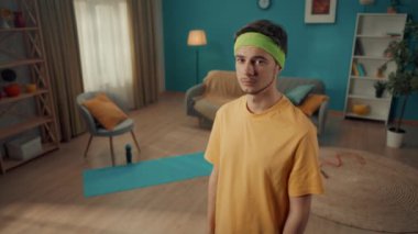 Spor kıyafetleri içinde genç bir adamın portresi ve ev çalışmasından sonra kafasında bandajla. Bir adam kollarını göğsünün üzerinden geçirir, başını sallar ve güven içinde oturma odasındaki kameraya bakar.