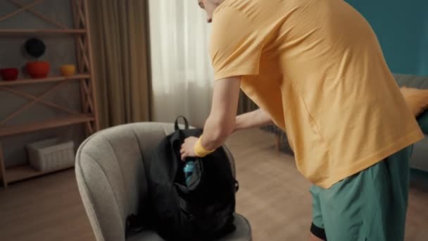 남자가 훈련을 가방을 있습니다 거실에서 배낭을 어깨에 운동복을 젊은이의 가손으로 — 비디오