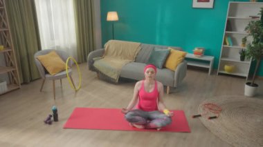 Genç ve çekici bir kadın lotus pozisyonunda gözleri kapalı oturur, yavaş yavaş nefes alır ve verir. Evde yoga yapan kızıl saçlı bir kadının portresi. Spor konsepti. Yoga, zen