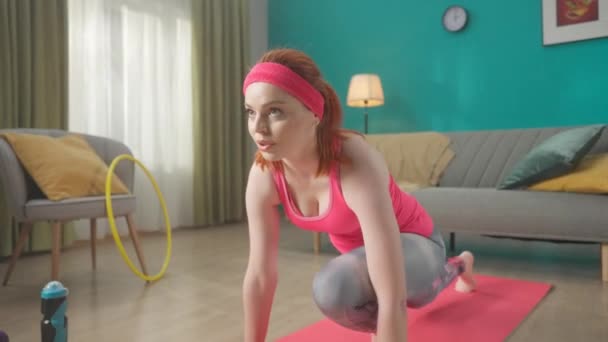 身穿粉色运动服的红头发年轻女子正在客厅里的一块运动垫上热身 家庭健身的概念 Hdr Bt2020 Hlg Material — 图库视频影像
