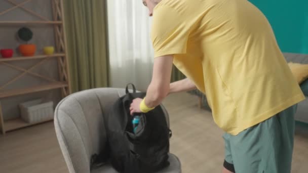 남자가 훈련을 가방을 있습니다 거실에서 배낭을 어깨에 운동복을 젊은이의 가손으로 — 비디오