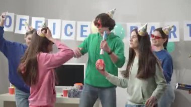 Bir grup neşeli şapkalı ve gözlüklü iş arkadaşı dans ediyor, eğleniyor, ortak bir başarıyı kutluyorlar, doğum gününü. Genç bir adam konfetiyle kraker patlatıyor. Ofisteki şirket. HDR BT2020