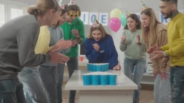 Tatil şapkalı ofis çalışanları bira pong oynarken eğleniyor. Genç bir kadın nişan alıyor, topu atıyor ve ıskalıyor. Meslektaşlar birlikte güler. Ofis partisi, ofiste eğlence. Ağır çekim. HDR