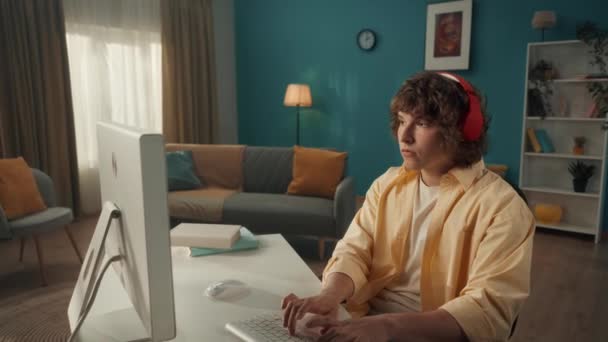 Kırmızı Kablosuz Kulaklıklı Genç Bir Kıvırcık Bilgisayar Başında Otururken Müzik — Stok video