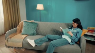 Asyalı kadın koltukta otururken hevesle kitap okuyor. Yanında kızıl kablosuz kulaklık takan kıvırcık saçlı genç bir adam ateş püskürüyor. Evde dinlenme konsepti, boş zaman. Yavaş