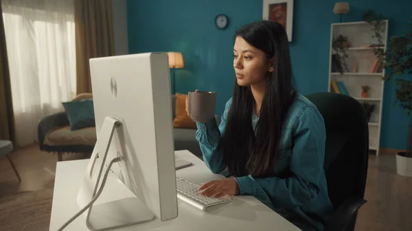 アジアの女性がコンピュータに座っている 一方では 女性はコーヒーのカップを保持し もう一方はキーボードを入力しています 女性の作品 電子メールを書きます メッセージ チャット インターネットサーフィン フリーランス — ストック写真