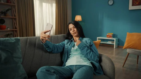 迷人的亚洲女人在智能手机上摆出一副自私自利的姿势 一个年轻的女人正坐在客厅的沙发上 手里拿着电话 — 图库照片