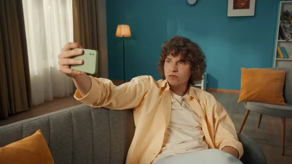一个年轻人用智能手机自私自利 客厅沙发上一个卷发男子的画像 手里拿着一部手机 — 图库照片