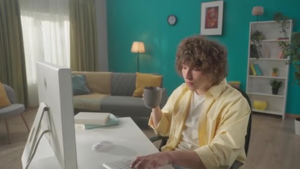 Joven Rizado Sienta Una Computadora Bebe Café Matutino Hombre Escribiendo — Vídeos de Stock