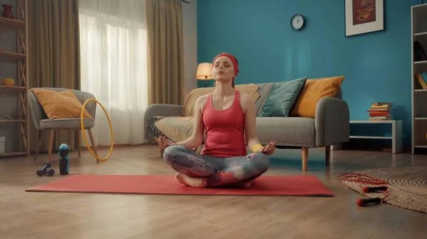 一位年轻貌美的女子盘腿坐在荷花的位置上 闭着眼睛 红头发 身穿粉色运动服 头戴头巾的女人在家里练习瑜伽 体育概念 瑜伽课 — 图库照片
