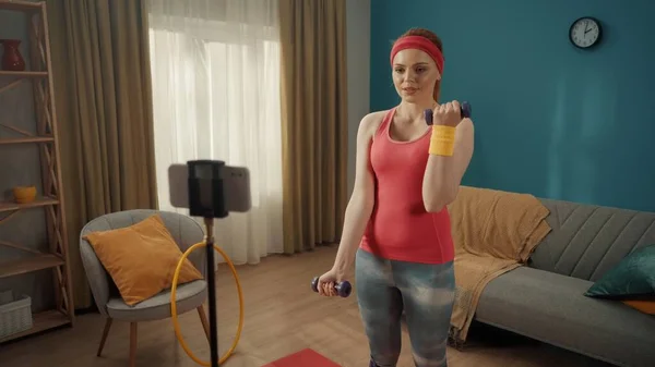 Młoda Sprawna Kobieta Ćwicząca Biceps Hantlami Domu Przed Telefonem Zamontowanym — Zdjęcie stockowe
