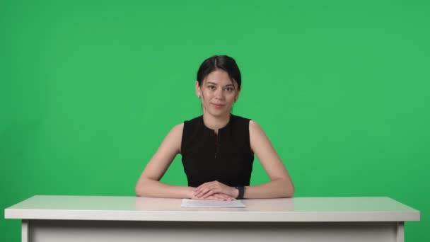 緑の画面の背景を持つテレビスタジオのライブニュース番組 女性のテレビプレゼンターは自信を持って話し その日の出来事をカバーします アジアの女性がテーブルに座り 紙から情報を読み取る ケーブル — ストック動画